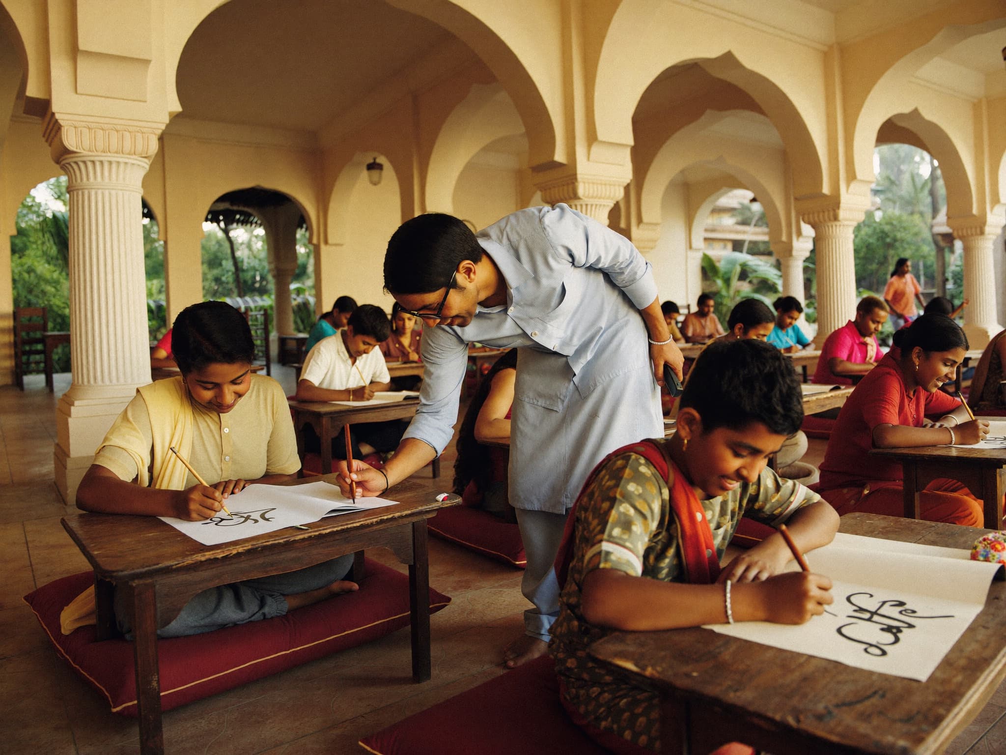 A mentor guiding young students practising calligraphy in a heritage courtyard workshop